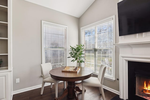 dining room with lofted ceiling, wood finished floors, baseboards, and a warm lit fireplace