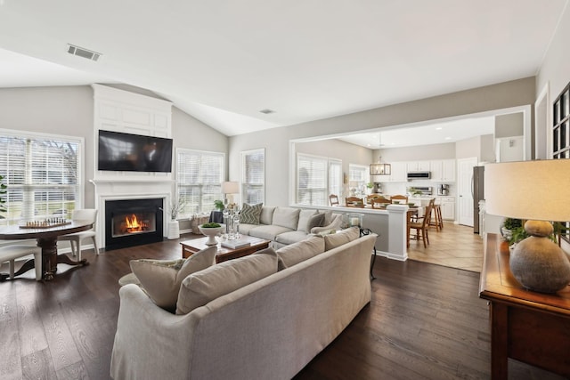 living room featuring dark wood-style floors, visible vents, a healthy amount of sunlight, and lofted ceiling