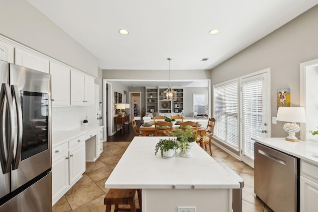 kitchen with visible vents, a kitchen island, white cabinets, appliances with stainless steel finishes, and decorative light fixtures