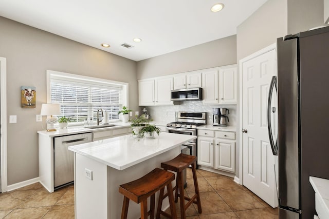 kitchen with a sink, backsplash, appliances with stainless steel finishes, and white cabinetry