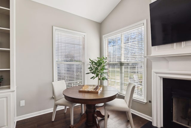 dining space with baseboards, lofted ceiling, wood finished floors, and a fireplace