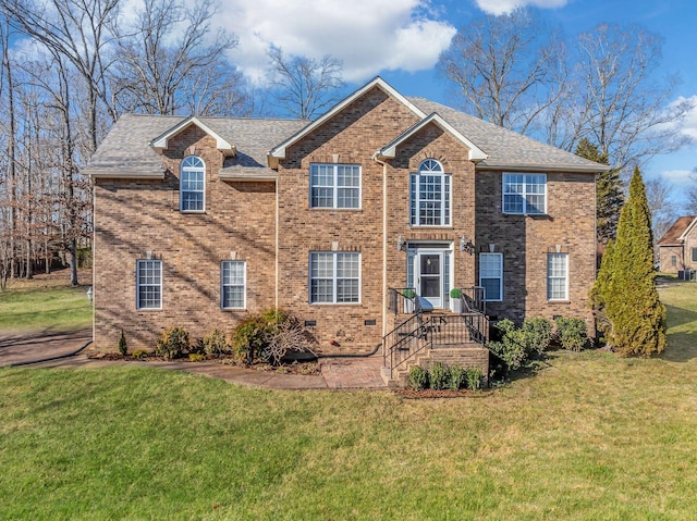 colonial home with brick siding, a front yard, and roof with shingles