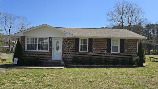 view of front of home featuring brick siding, a shingled roof, a front lawn, and fence