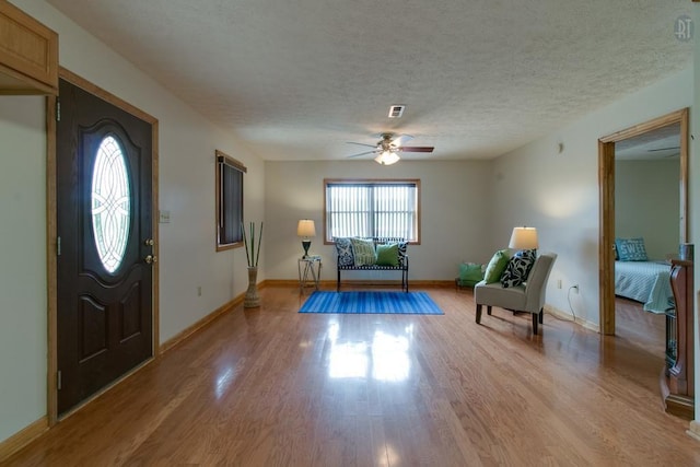 foyer featuring a ceiling fan, visible vents, baseboards, light wood-style floors, and a textured ceiling