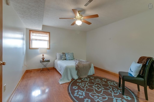 bedroom with wood finished floors, visible vents, baseboards, ceiling fan, and a textured ceiling