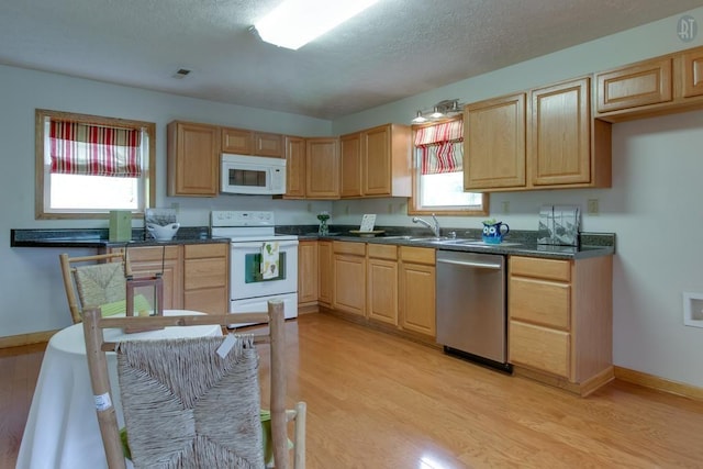 kitchen with light brown cabinetry, light wood finished floors, white appliances, and a sink