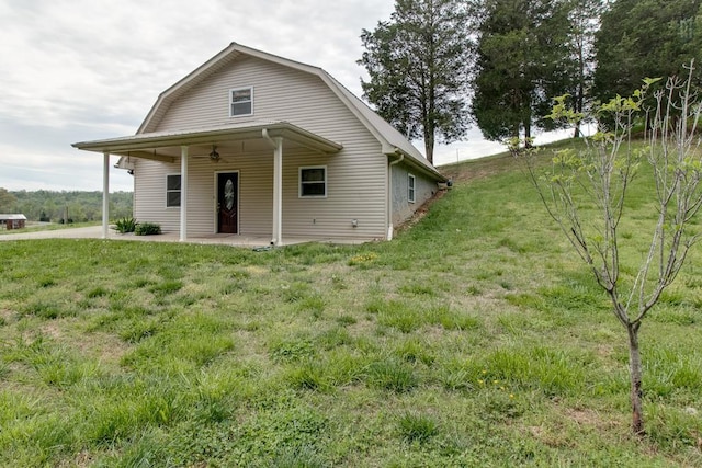 rear view of property featuring a gambrel roof, a lawn, and a patio area