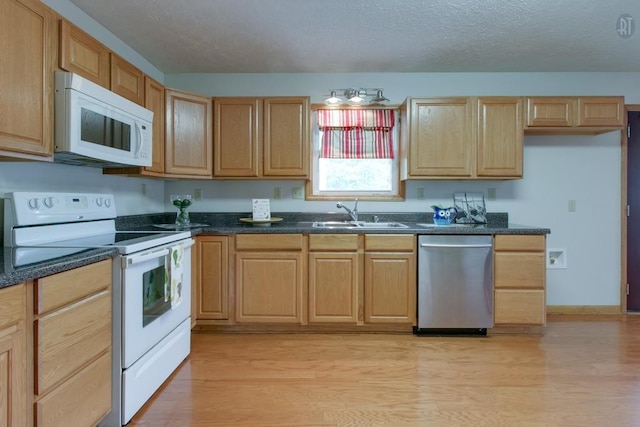 kitchen with light wood finished floors, light brown cabinets, white appliances, a textured ceiling, and a sink