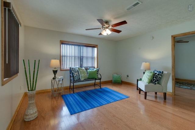 living area featuring ceiling fan, wood finished floors, visible vents, and baseboards