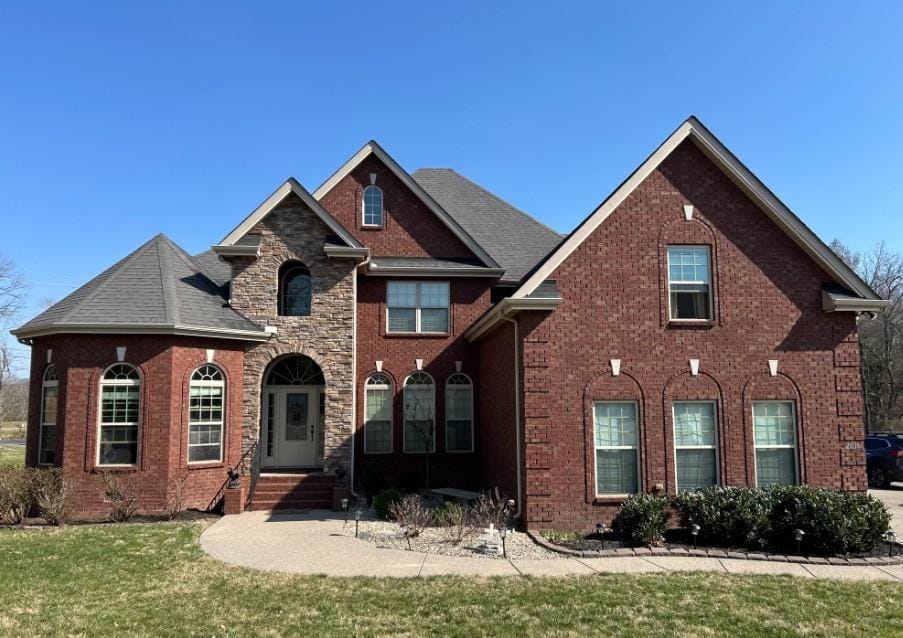 view of front facade featuring stone siding, brick siding, a front yard, and a shingled roof