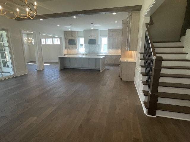 kitchen featuring backsplash, decorative light fixtures, a center island with sink, light countertops, and dark wood-style flooring