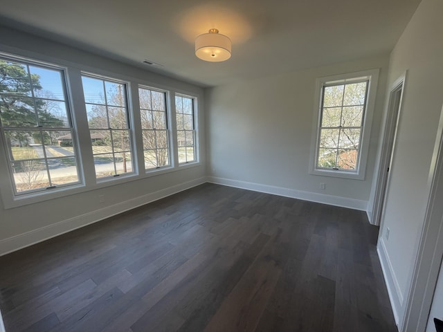 spare room featuring a wealth of natural light, visible vents, dark wood finished floors, and baseboards