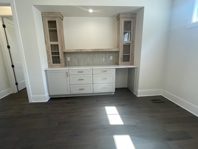 kitchen with baseboards, dark wood finished floors, light countertops, glass insert cabinets, and tasteful backsplash