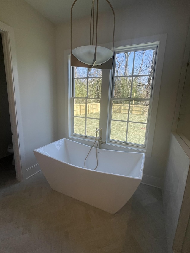 full bathroom featuring baseboards, a freestanding bath, and toilet