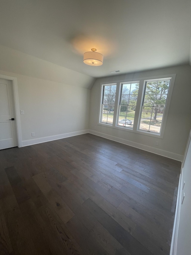 empty room featuring dark wood finished floors, baseboards, and lofted ceiling