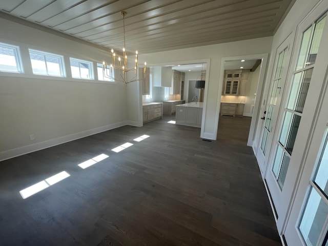 unfurnished dining area featuring baseboards, dark wood-type flooring, an inviting chandelier, and a sink