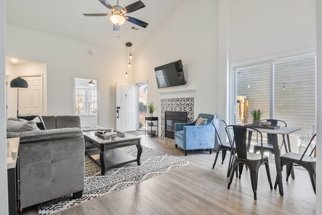 living area featuring a ceiling fan, wood finished floors, a fireplace, and high vaulted ceiling