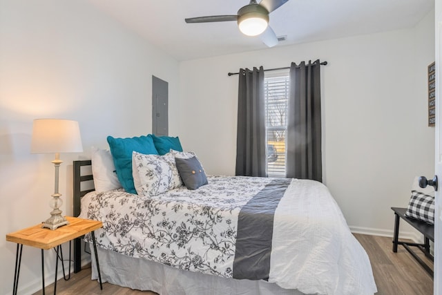 bedroom with electric panel, wood finished floors, baseboards, and ceiling fan