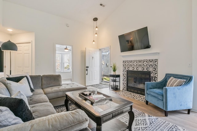 living area with a tiled fireplace, visible vents, light wood finished floors, and high vaulted ceiling