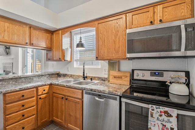 kitchen with a sink, appliances with stainless steel finishes, brown cabinetry, and pendant lighting