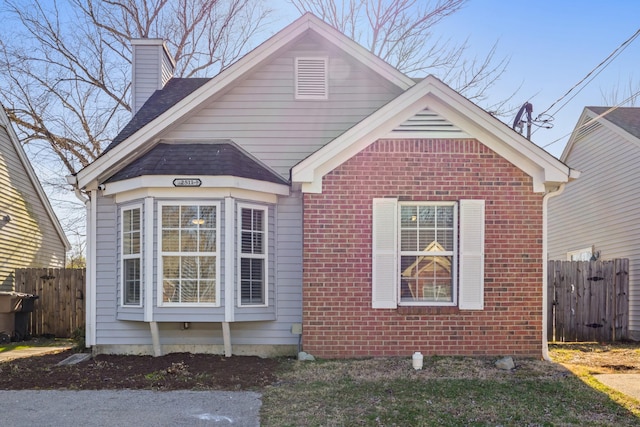 view of front facade featuring brick siding, a chimney, and fence