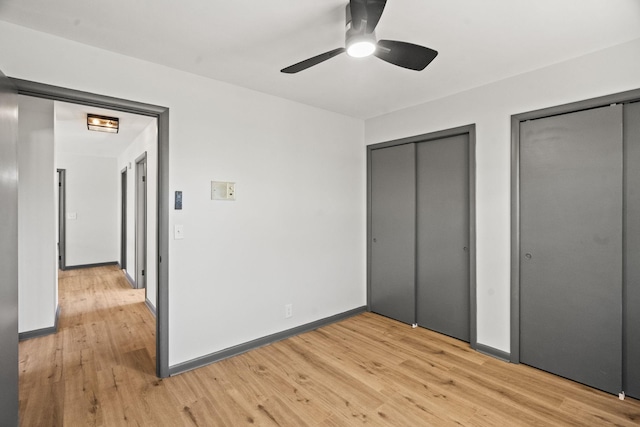 unfurnished bedroom with a ceiling fan, baseboards, multiple closets, and light wood finished floors