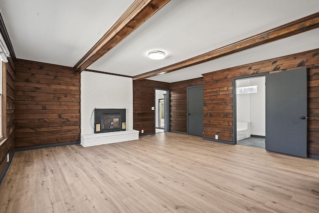 unfurnished living room featuring beam ceiling, wooden walls, light wood-style flooring, and a brick fireplace