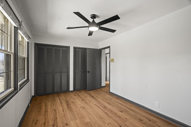 unfurnished bedroom with wood finished floors, baseboards, two closets, and ceiling fan