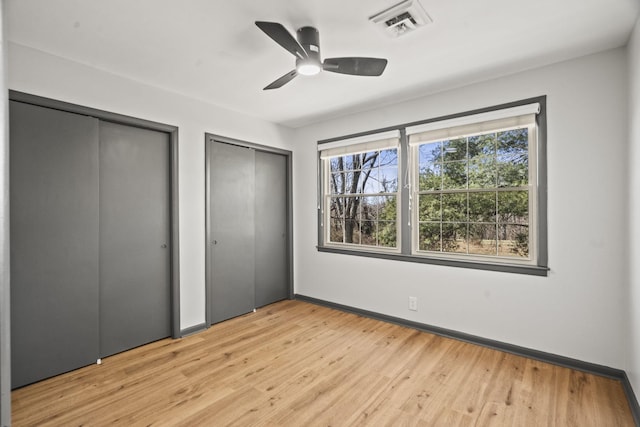 unfurnished bedroom with visible vents, two closets, a ceiling fan, light wood finished floors, and baseboards