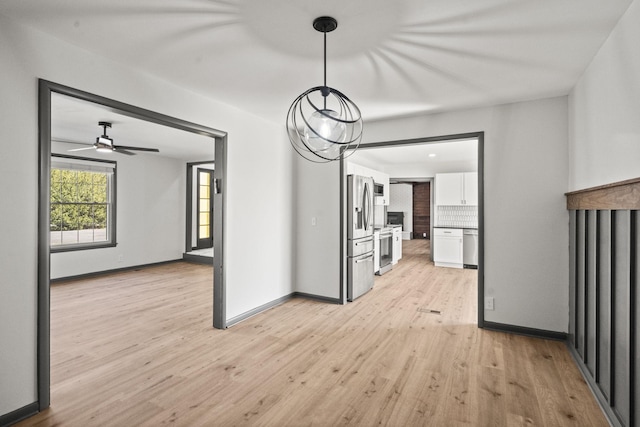 unfurnished dining area with light wood finished floors, an inviting chandelier, and baseboards