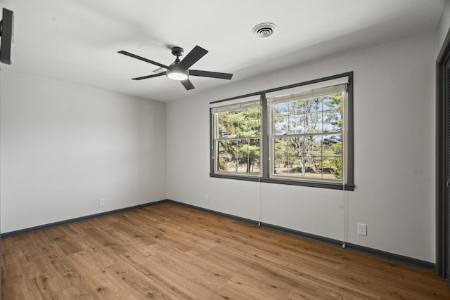 spare room with a ceiling fan, wood finished floors, visible vents, and baseboards