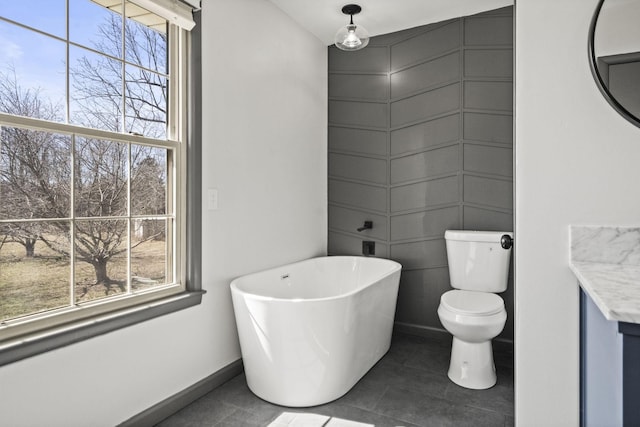 full bath featuring a freestanding tub, toilet, a healthy amount of sunlight, and tile patterned flooring