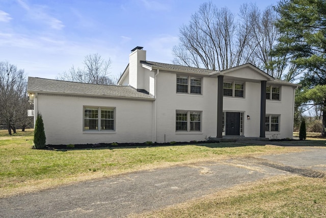 view of front facade featuring a front yard, brick siding, a chimney, and a shingled roof