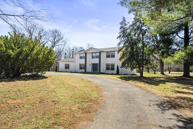 view of front of house featuring aphalt driveway, stucco siding, a chimney, and a front lawn