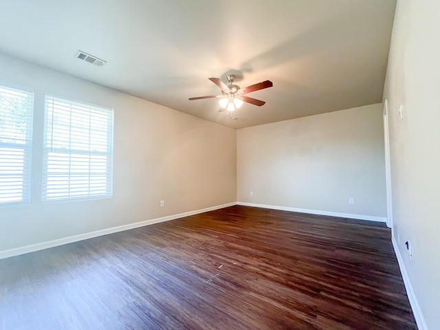 empty room with a ceiling fan, dark wood-style floors, visible vents, and baseboards