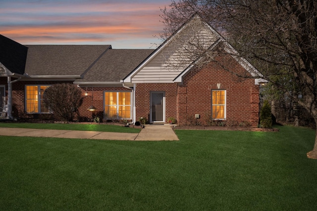 view of front of property featuring brick siding, a yard, and roof with shingles