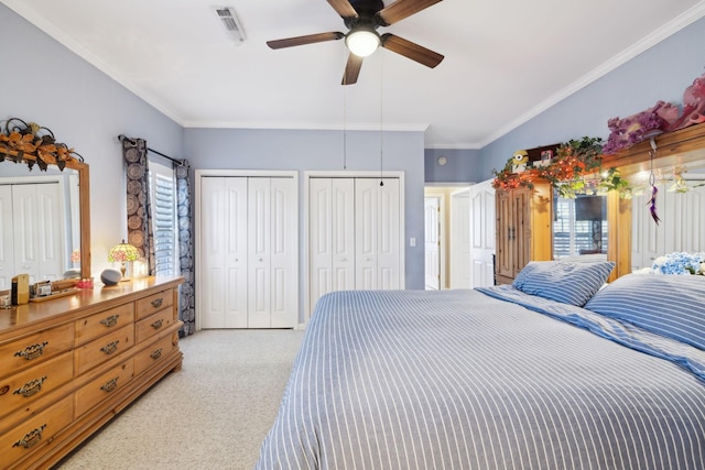 bedroom with visible vents, light carpet, two closets, and ornamental molding