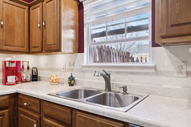 kitchen with a sink, backsplash, brown cabinetry, and light countertops