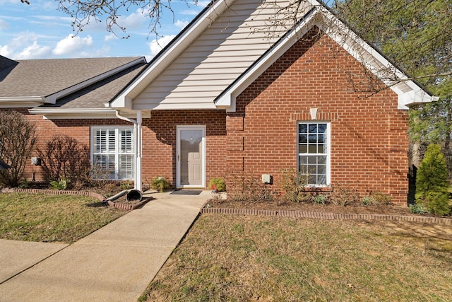 view of front of home with a front yard, brick siding, and roof with shingles