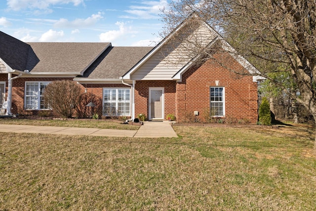 view of front facade with brick siding, roof with shingles, and a front lawn