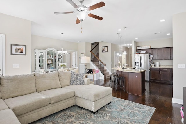 living room with ceiling fan with notable chandelier, dark wood finished floors, recessed lighting, baseboards, and stairs