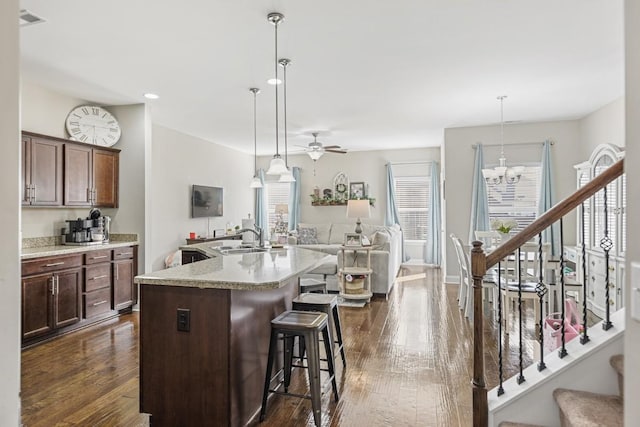 kitchen featuring dark wood finished floors, open floor plan, a kitchen bar, ceiling fan with notable chandelier, and a sink