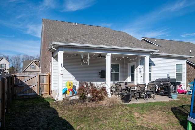 rear view of property featuring a shingled roof, fence, a patio, and a gate