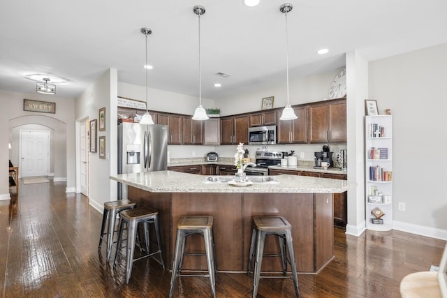 kitchen featuring stainless steel appliances, arched walkways, dark brown cabinets, and a breakfast bar area