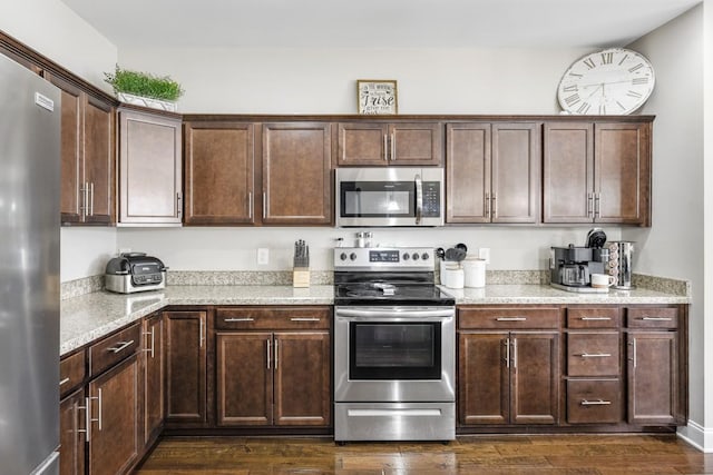 kitchen with dark brown cabinets, appliances with stainless steel finishes, dark wood-type flooring, and light stone countertops