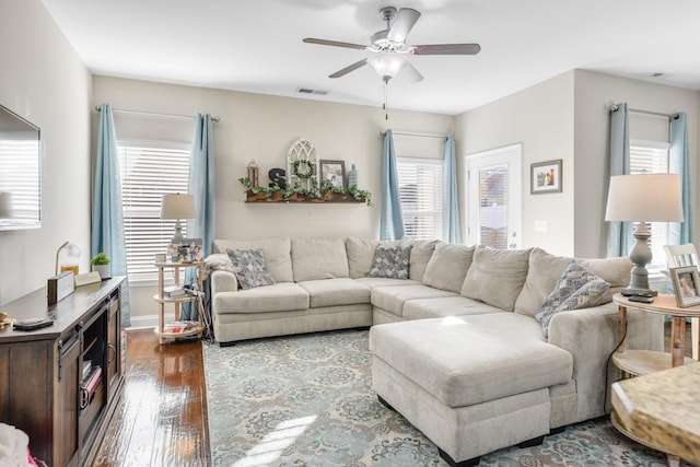 living area featuring dark wood-type flooring, a ceiling fan, visible vents, and baseboards