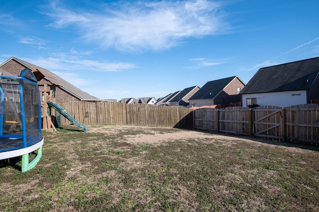 view of yard with a playground, a trampoline, a fenced backyard, and a gate