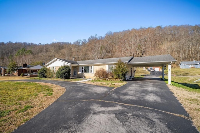 view of front of property featuring an attached carport, a front yard, a forest view, and driveway