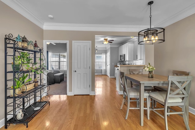 dining space featuring light wood-style flooring, ceiling fan with notable chandelier, baseboards, and ornamental molding