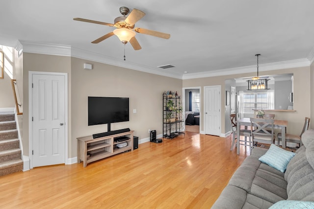 living room with wood finished floors, visible vents, a ceiling fan, stairs, and crown molding